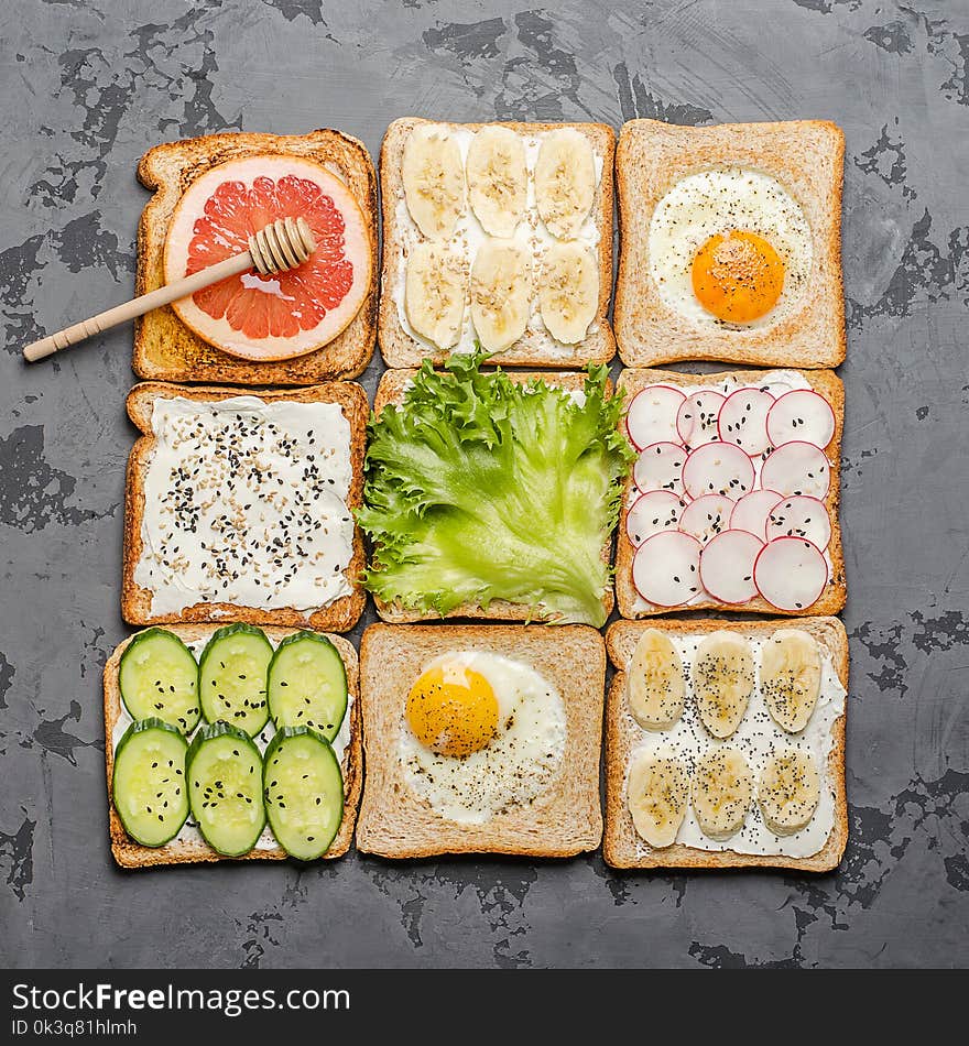 Different toasts on a gray background. Toast with egg, banana, salad, cream cheese, cucumber, radish, grapefruit and honey.