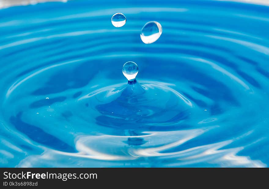 A falling drop in the blue water. The waves diverge from the drop.