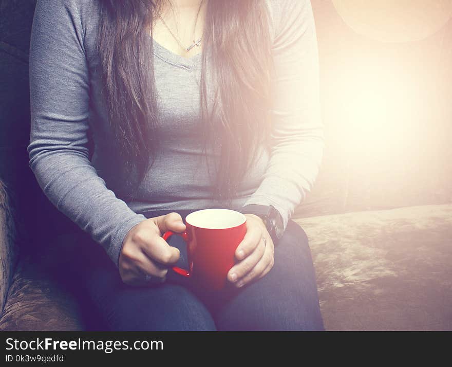 The girl is sitting on the couch and drinking a hot drink