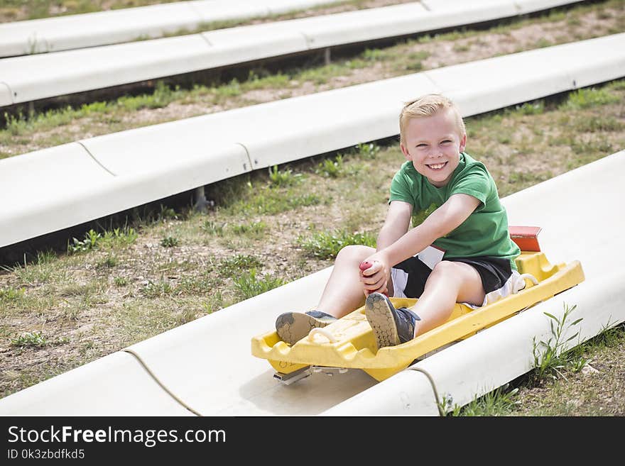 Cute smiling young boy riding downhill on an alpine coaster ride outdoors on a summers day. Happy and having fun on a thrilling theme park ride. Cute smiling young boy riding downhill on an alpine coaster ride outdoors on a summers day. Happy and having fun on a thrilling theme park ride