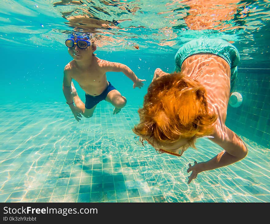 Two children diving in masks underwater in pool.