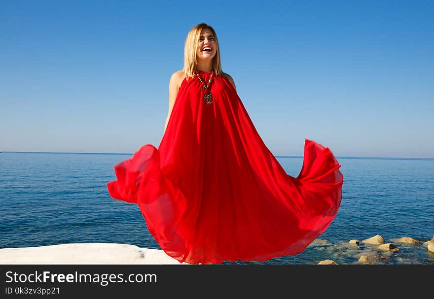 Woman in the red dress on the white stone at the beach in Cyprus. Woman in the red dress on the white stone at the beach in Cyprus.