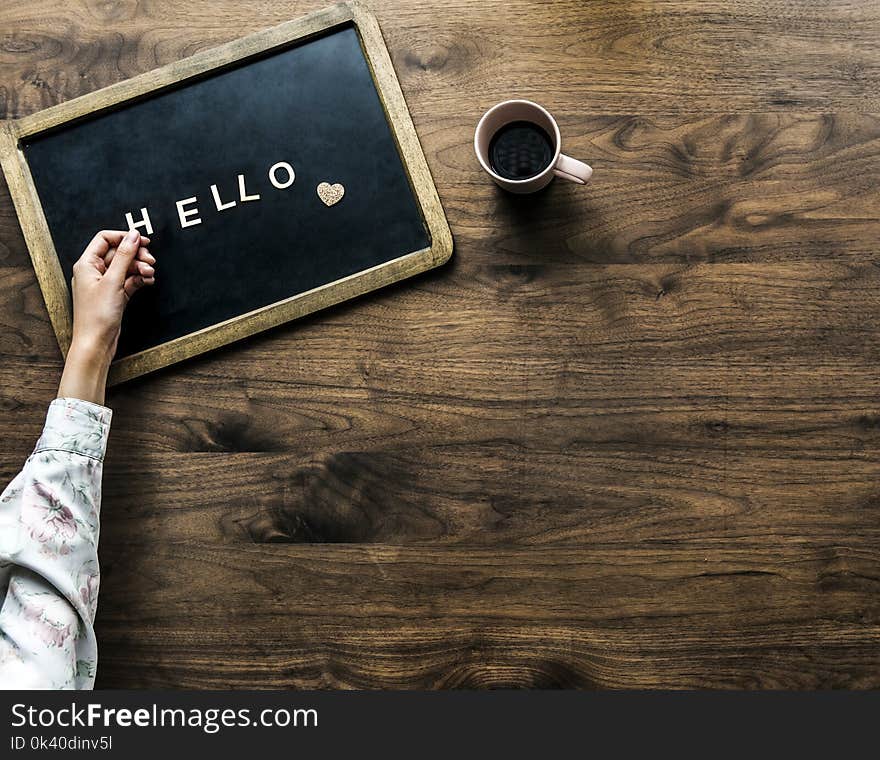 Person&#x27;s Hand on Black Board With Hello Text Beside Brown Mug