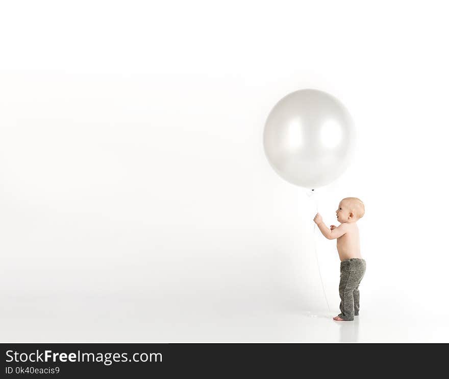 Baby in Black Pants Holding White Balloon While Standing