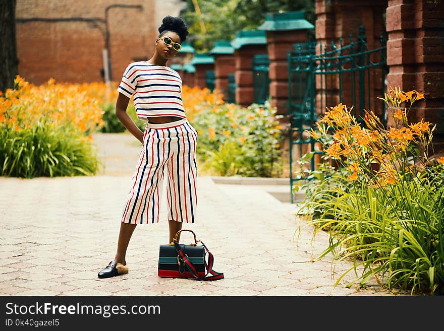 Woman Wearing White, Black, and Red Striped Crew-neck T-shirt With Matching Pants Standing Outside Beside Black Leather 2-way Bag