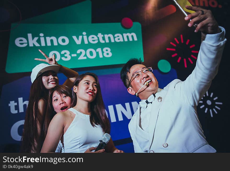 Man in White Suit Jacket Holding Phone in Front of Three Women