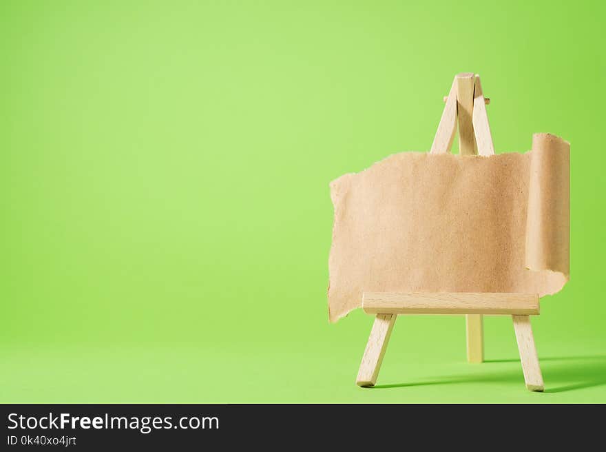 Small easel with blank paper on green background. Torn sheet of paper on easel. Place for your text.