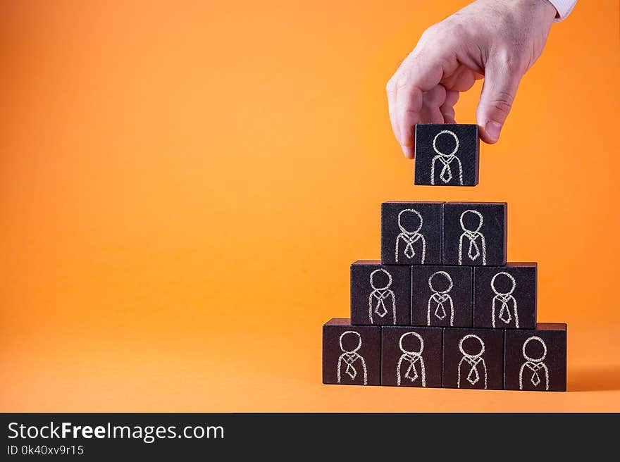 Man`s hand holding a top of wooden blocks pyramid over wooden table. Business concept for human resources, corporate hierarchy, social networking, career success, promotion and management concept. Man`s hand holding a top of wooden blocks pyramid over wooden table. Business concept for human resources, corporate hierarchy, social networking, career success, promotion and management concept.