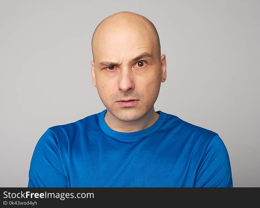 Serious bald man with raised eyebrow looking at camera. Displeased guy isolated over grey background