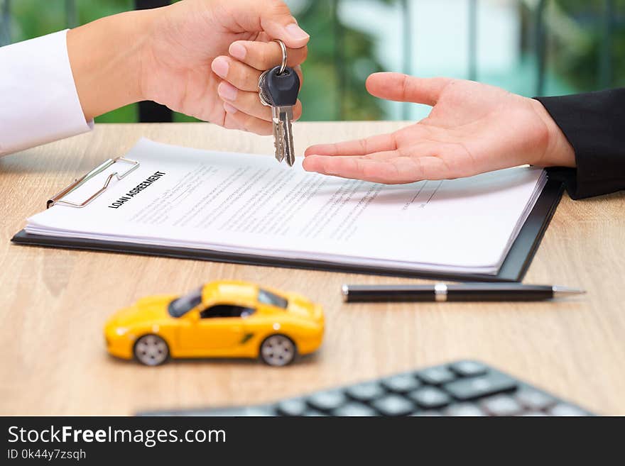 Businessman giving car key over loan agreement document with car toy and calculator on wooden desk