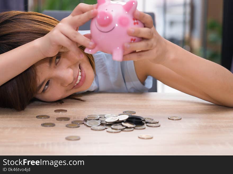 Asian woman picking out money of piggy bank on wooden desk.