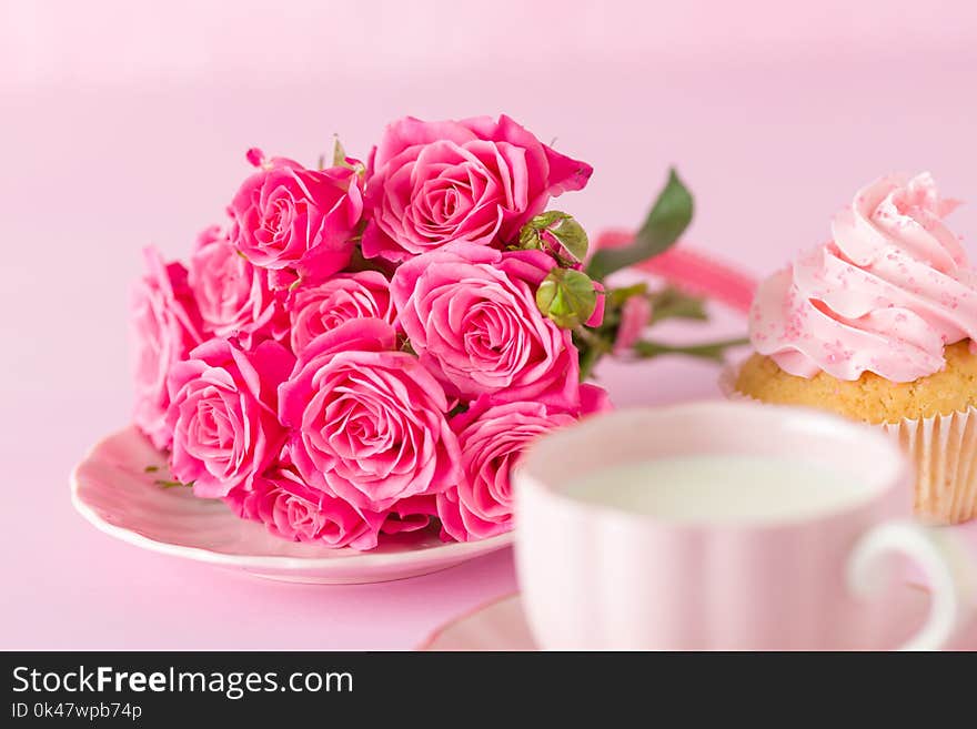 Cupcake with pink cream decoration and roses on pink pastel background.