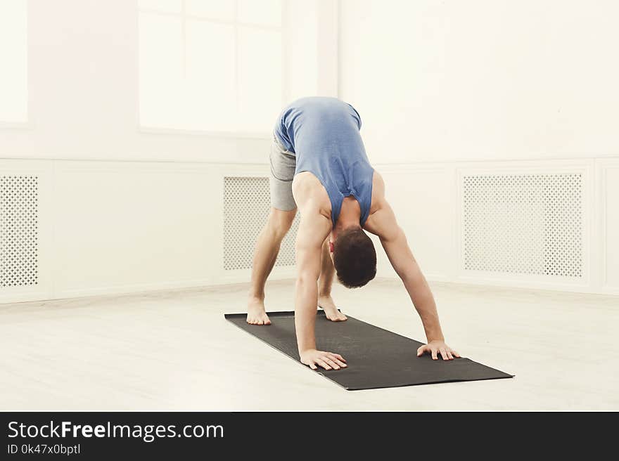 Man training yoga in dog pose in gym at white background, copy space. Young boy makes exercise, fitness, meditation, front view. Man training yoga in dog pose in gym at white background, copy space. Young boy makes exercise, fitness, meditation, front view