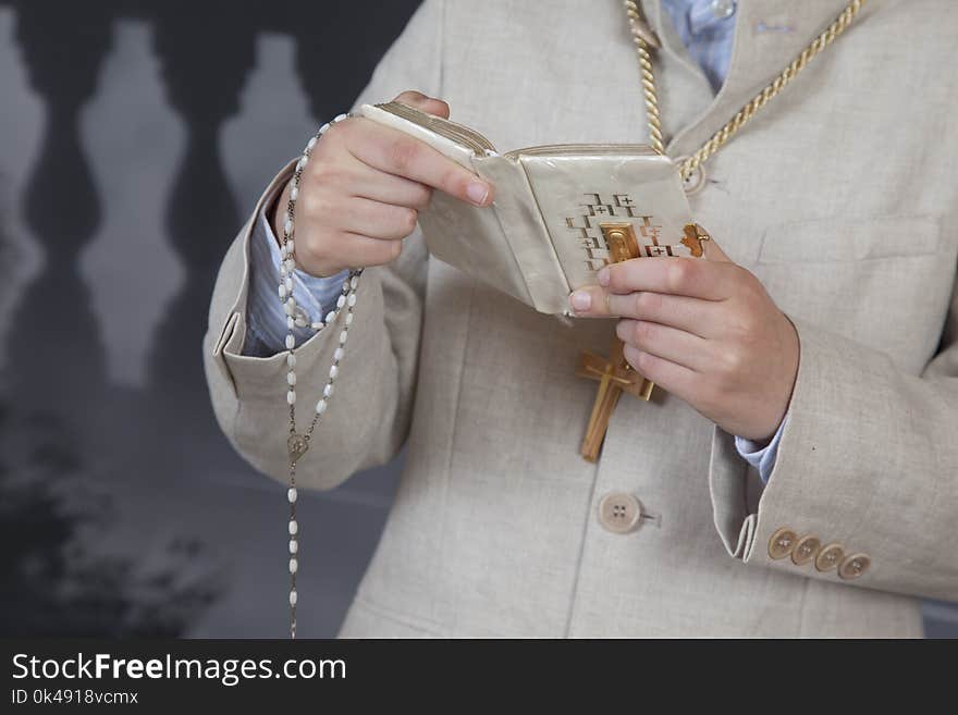 Detail of the hands of a communion child dressed in a beige suit and holding a book and a rosary