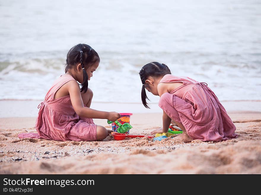 Two cute asian little child girls having fun to play with sand on beach together in summer vacation