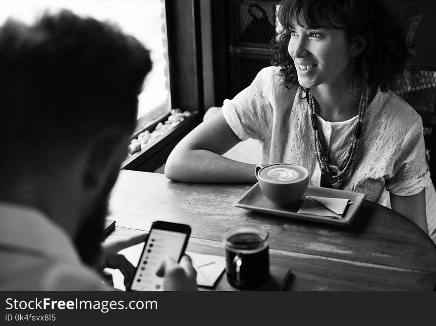 Grayscale Photography of Man and Woman Sitting Beside Wooden Table