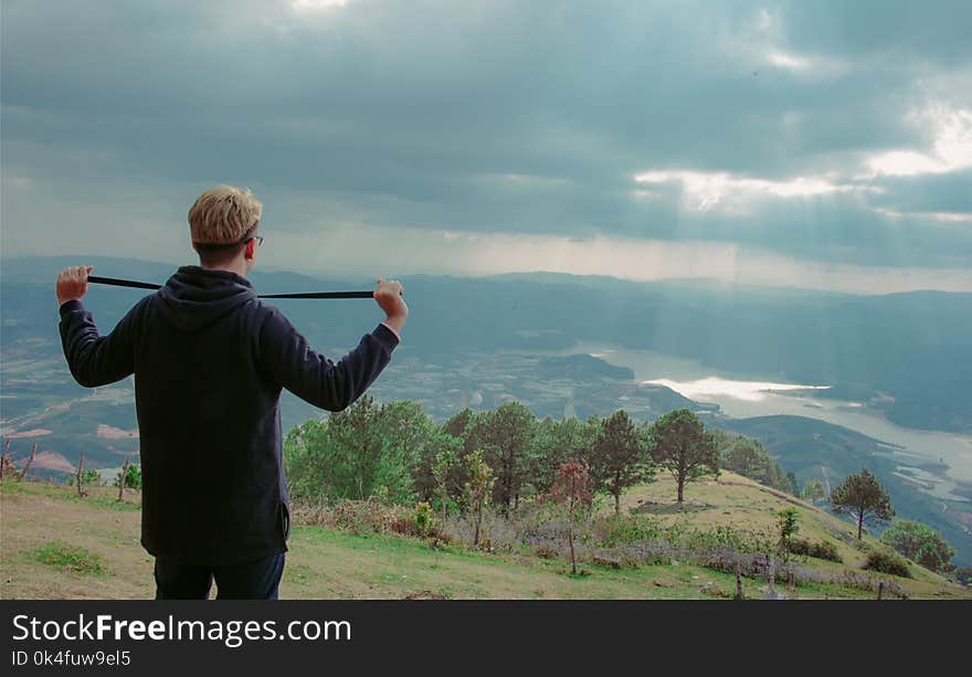 Man Wearing Hoodie Standing on Mountain Under Cloudy Sky