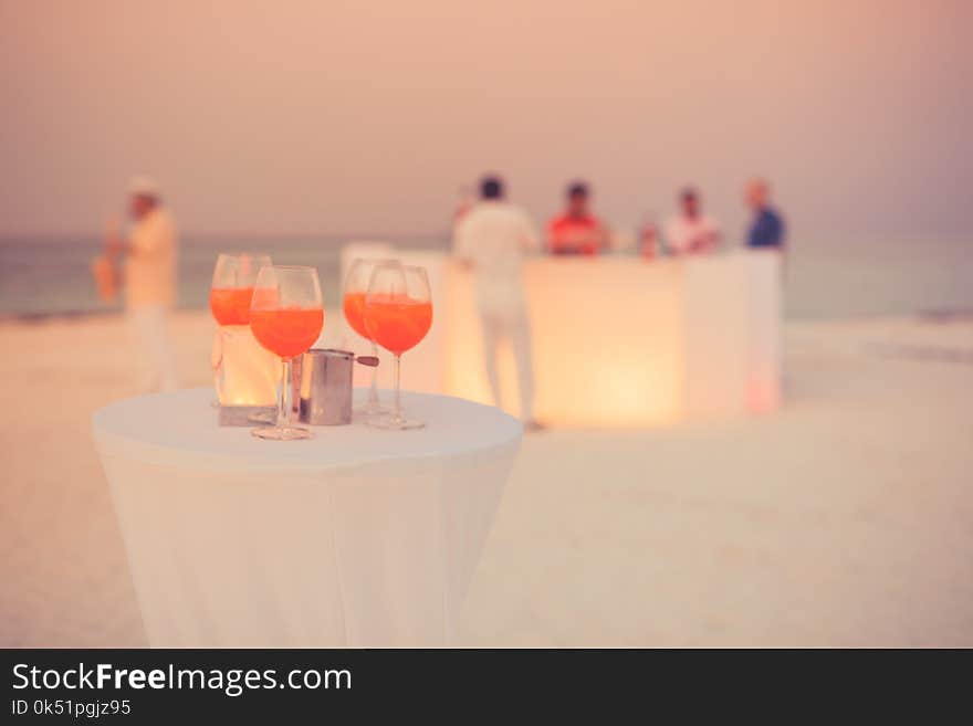 Aperol cocktail glasses on simple white table. Beach party background with drinks and blurred people in background