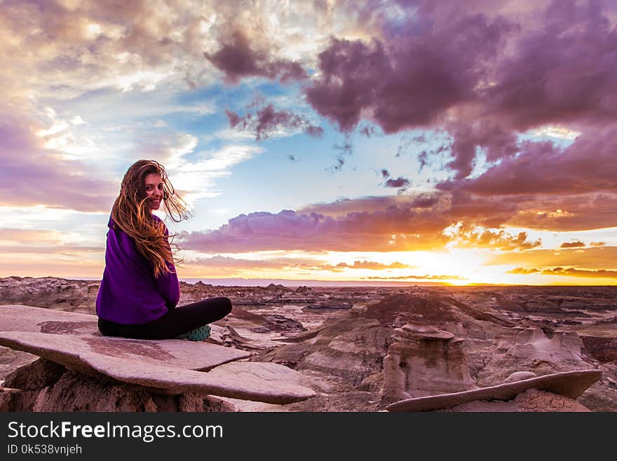 Woman Sits on Mountain Under Cloudy Sky at Sunset