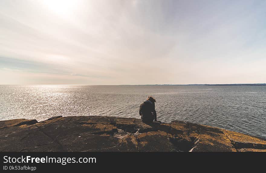 Person Sitting on Stone in Front of Sea Water