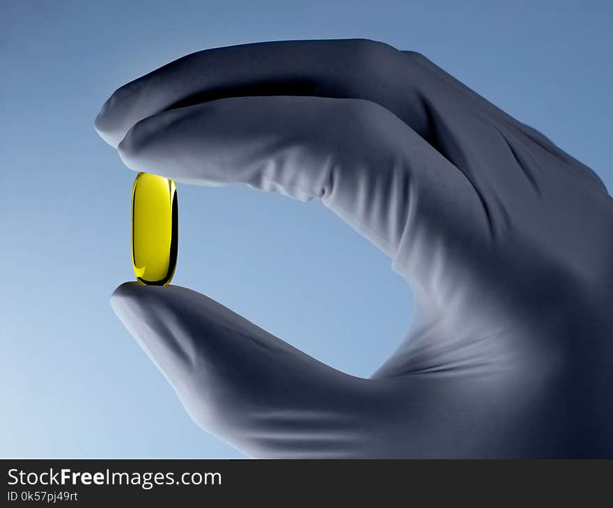 Hand with glove holding a pill on blue