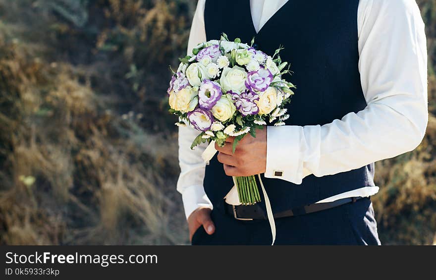 Wedding. The groom in a white shirt and waistcoat are holding bouquets of of white roses, hypericum, lisianthus, chrysanthemum, eustoma