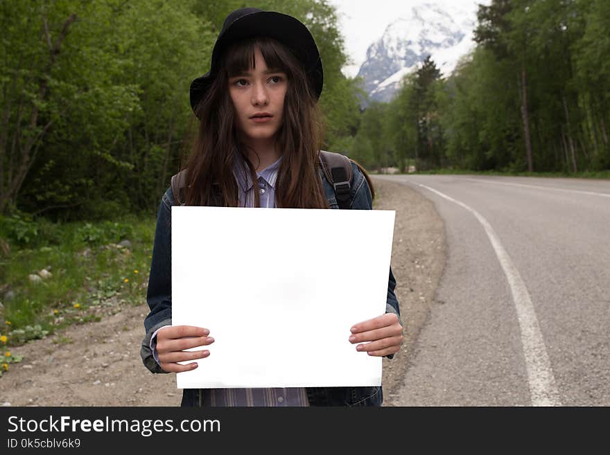 Your text here.Travel and hitch-hiking concept. Studio portrait of happy pretty young woman standing with empty blank.