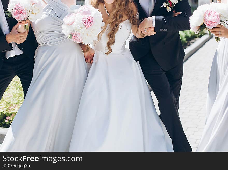 Gorgeous bride with peony bouquet and stylish groom posing in sunny garden with bridesmaids and groomsmen on wedding day. luxury wedding couple having fun with friends