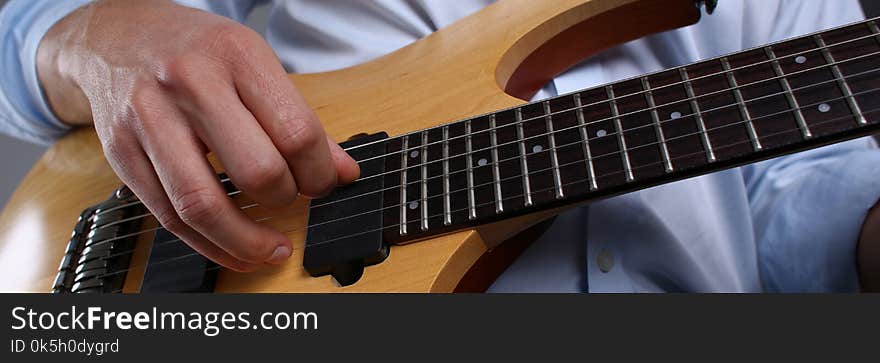 Male arms holding and playing classic shape wooden electric guitar closeup. Six stringed learning musical school education art leisure electrical vintage stage shop having fun enjoying hobby concept. Male arms holding and playing classic shape wooden electric guitar closeup. Six stringed learning musical school education art leisure electrical vintage stage shop having fun enjoying hobby concept