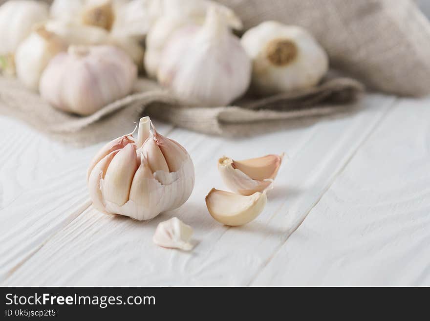 Garlic bulbs with garlic cloves with canvas on white rustic wood.