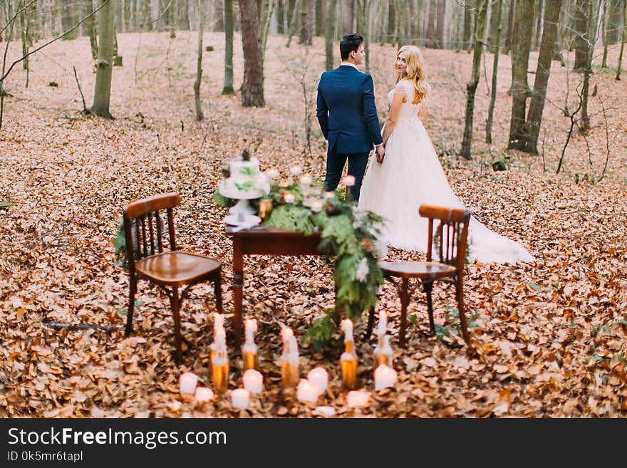 Beautiful Wedding Couple Holding Hands Near The Vintage Table In Autumn Forest