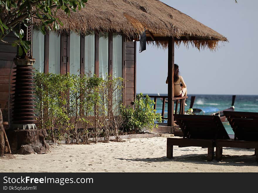 Portrait young asian female brown bikini sitting in front of luxury nature resident on idyllic beach shore turn back