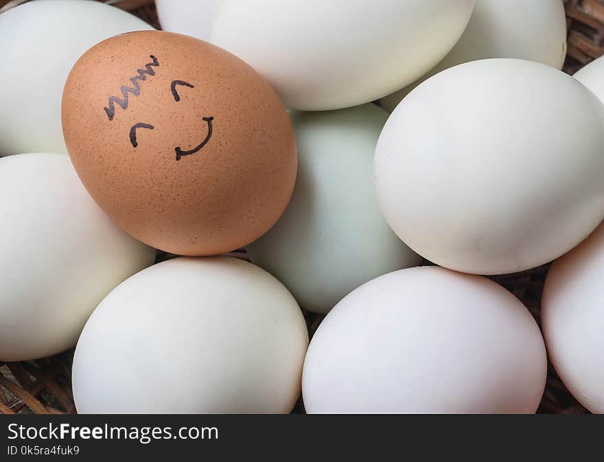 Closeup surface brown chicken egg with paint in smile face on pile of white duck egg on wood basket background