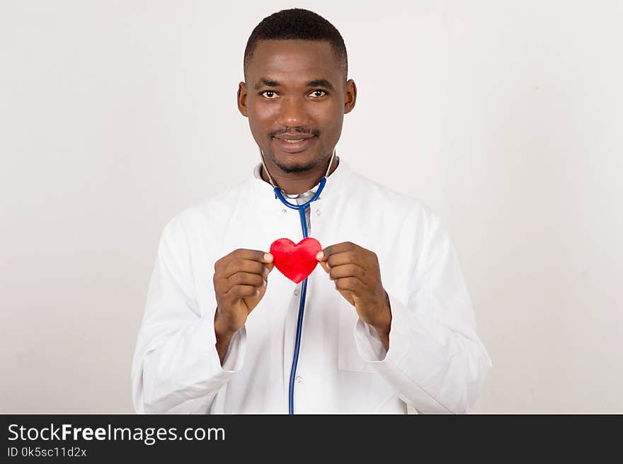 Positive male doctor standing with stethoscope and red heart symbol on light background. Positive male doctor standing with stethoscope and red heart symbol on light background.