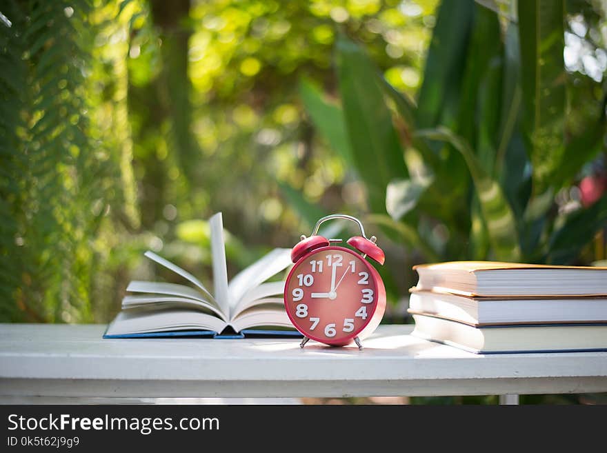 Red alarm clock with book on home nature garden background.