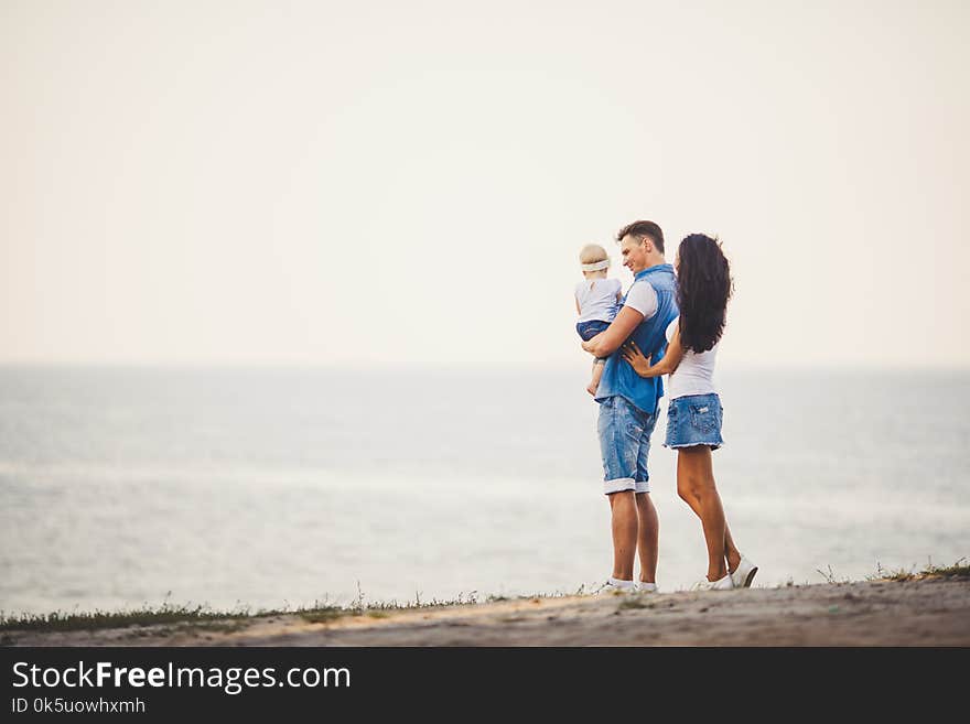 Family holiday in nature. Three, Mom, Dad, daughter one year standing with backs on cliff overlooking sea. man holding hild in arm