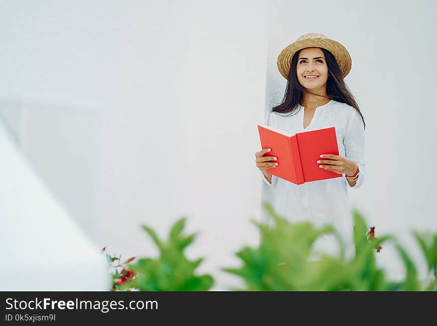 Young and pretty girl in a summer city standing near white wall with red book. Young and pretty girl in a summer city standing near white wall with red book