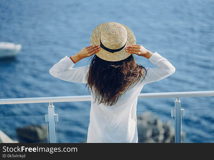 A beautiful young girl in a straw hat standing on a summer terrace and looking at the ocean. A beautiful young girl in a straw hat standing on a summer terrace and looking at the ocean