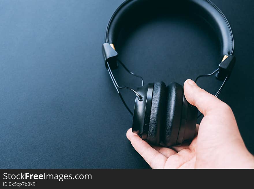 Wireless headphone is hold or hanging by a man right hand with black background and copy space for text. Wireless headphone is hold or hanging by a man right hand with black background and copy space for text