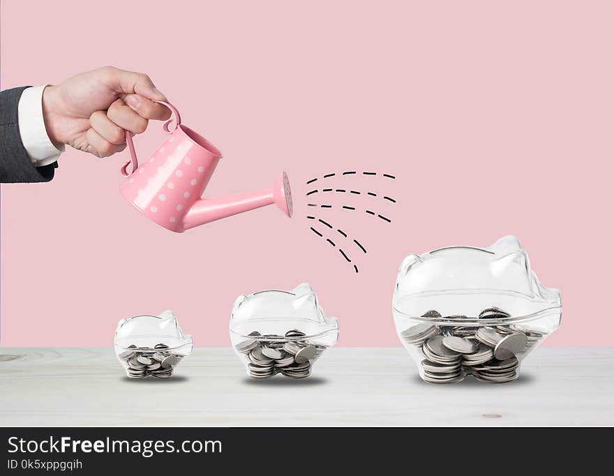 Transparent piggy bank filled with coins on wood background.Saving investment colorful concept.Watering can and money growth draw