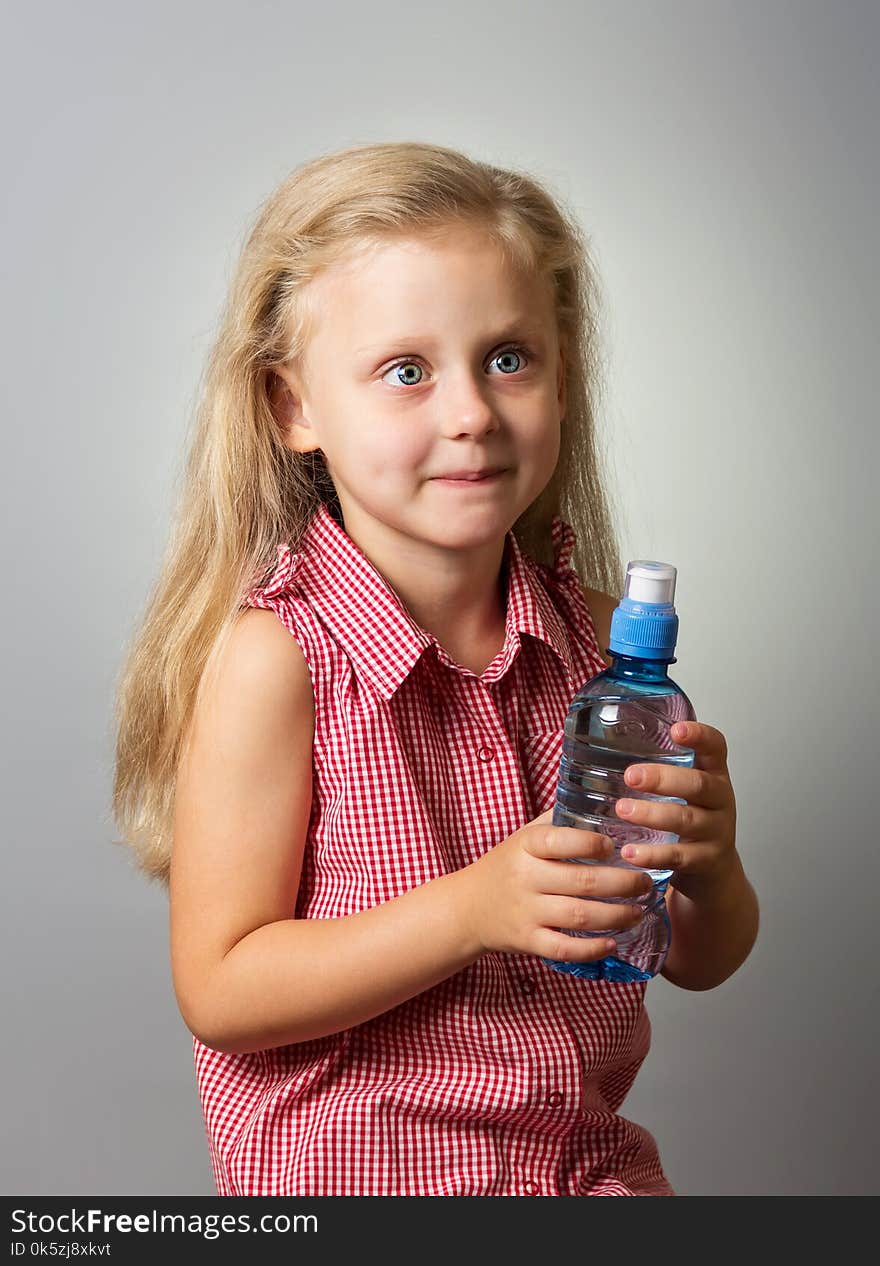 Adorable little girl with long hair holding a bottle of water on gray background