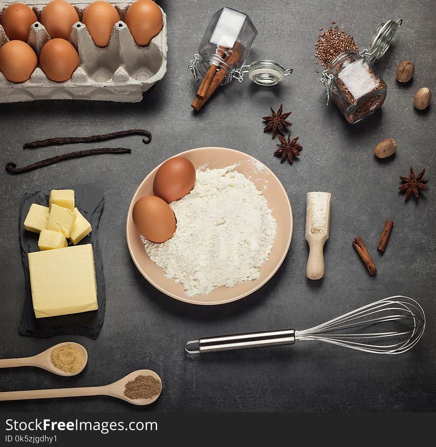 Flour and eggs in bowl, foods and spices on desktop, on grey