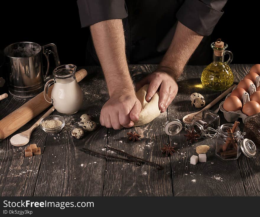 On table food and cooking utensils, dough in hands of Baker, isolated on black background