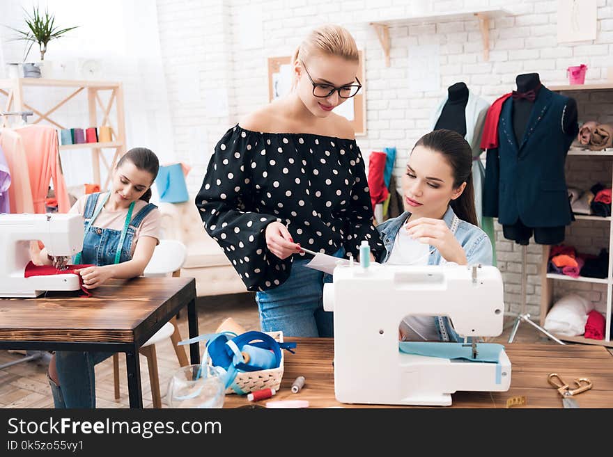 Three women at garment factory. They are happy and fashionable. They are sitting behind sewing machines. Three women at garment factory. They are happy and fashionable. They are sitting behind sewing machines.