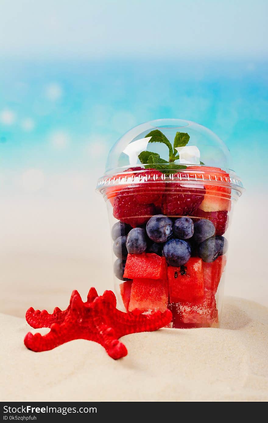 Plastic cup full of fresh cut fruits and berries on the sea coast. Paradise vacations concept. Copy space