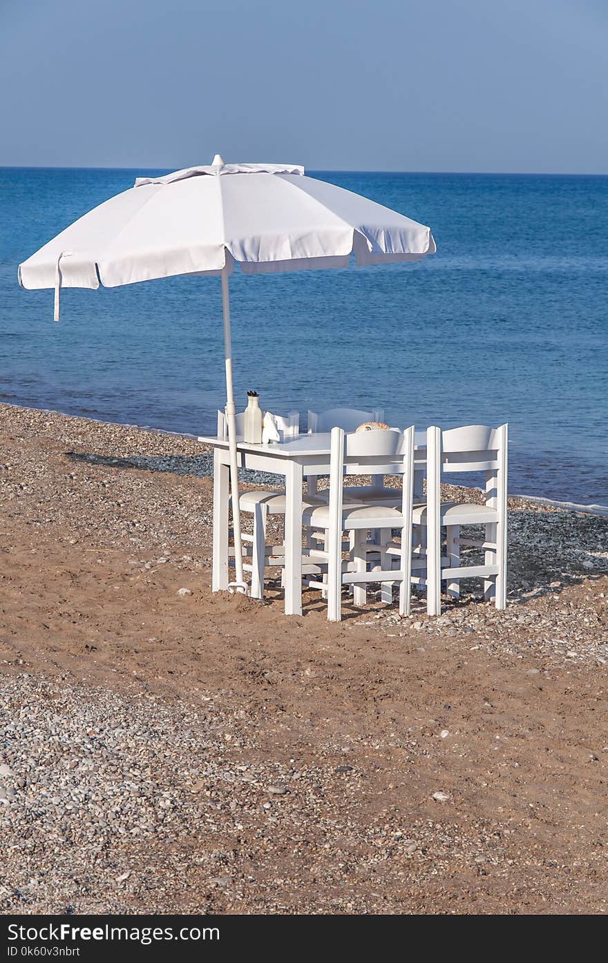 White wooden table with four chair and umbrella on beach with blue sea