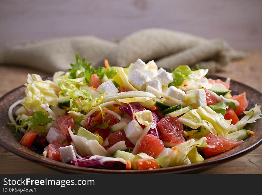 Healthy vegetarian food: citrus grapefruit, tomato, lettuce and cucumber salad with feta cheese in bowl on wooden table. horizontal