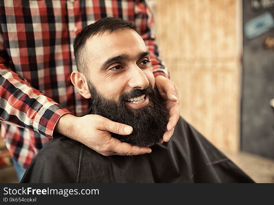 Smiling satisfied hipster client visiting barber shop, looking g