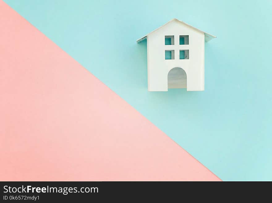 Miniature white toy house on pink and blue pastel color paper geometric flat lay background. Mortgage property insurance dream home concept. Miniature white toy house on pink and blue pastel color paper geometric flat lay background. Mortgage property insurance dream home concept