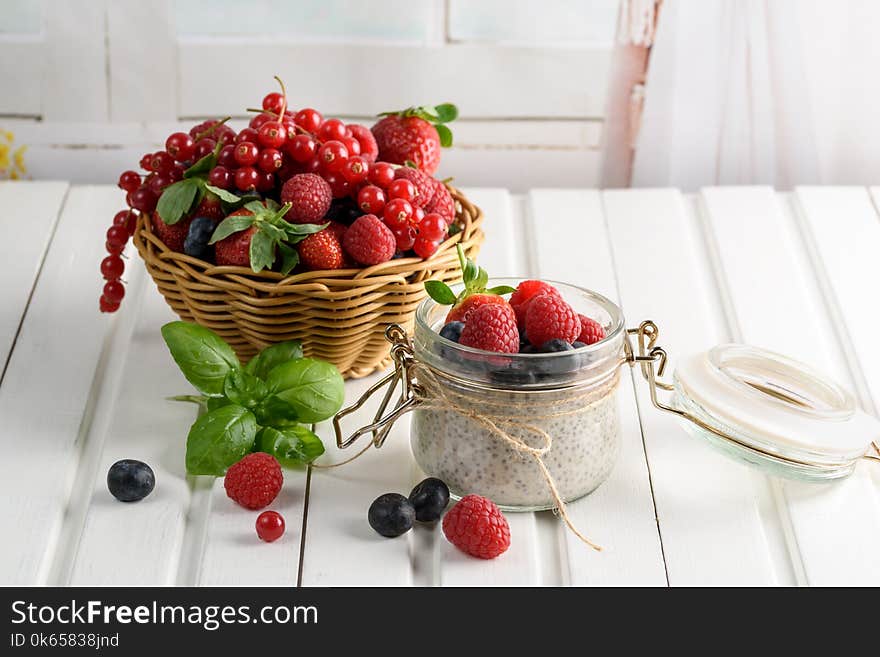 Healthy blended smoothie made from almond milk. Glass jar with chia pudding with fresh strawberries, raspberries and blueberries. Basket with berries. On a wooden light background.